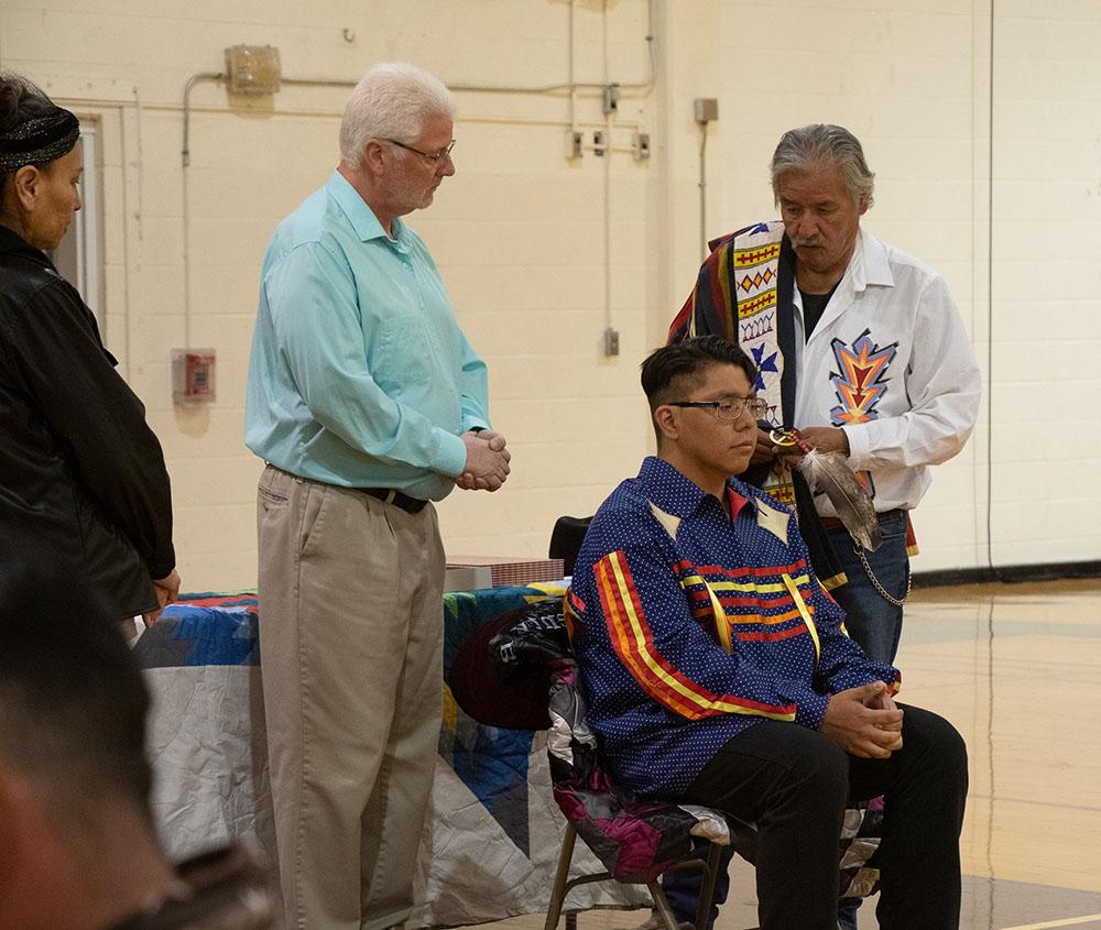 Three adult males in feather tying ceremony